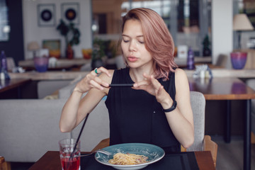 Attractive woman makes a photo of a carbonara paste in a cafe.