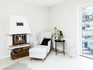fire in the fireplace by the relaxing chair in a white light room 
