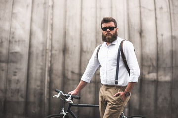 Fototapeta na wymiar serious fashionable bearded man in sunglasses standing with bicycle