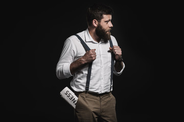 fashionable man in white shirt and suspenders standing with business newspaper in pocket isolated on black