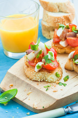 Bruschetta with tomato, bacon, matsarela and parsley on a wooden plate, a cup of orange juice on a blue tablecloth. Close-up. Italian appetizer.