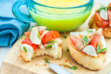 Bruschetta with tomato, bacon and parsley matsarela in the process of eating, a cup of orange juice on a blue tablecloth. Close-up. Breakfast. Italian appetizer.
