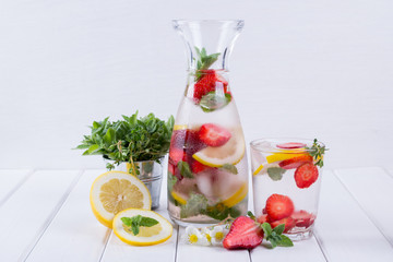 Mineral infused water with strawberry, ice, herb and mint leaves on white background, homemade detox soda water recipe.