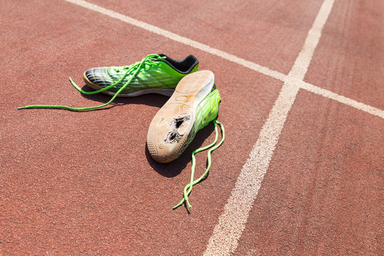A pair of broken green running shoes with big holes in the sole laying on a running track