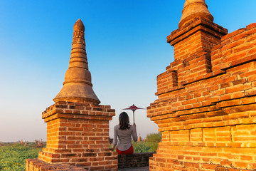 A girl with a traditional Burmese umbrella relaxing in an ancient temple during sunset, Bagan,Myanmar.Ancient temples in Bagan in sunny sunset.Young traveller enjoying a looking at Buddhist stupas.