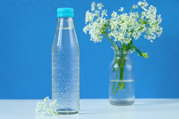 Glass bottle with clean drinking water on the table. A bouquet of wild flowers in the background....
