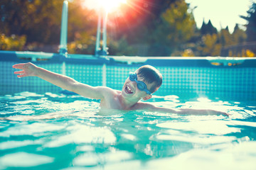 Happy little kid swimming in pool outdoor color graded sunset