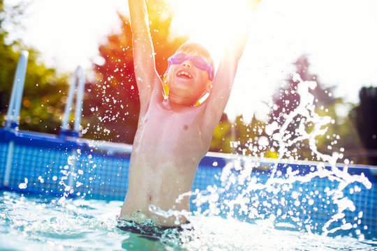 Happy little boy jumping in swimming pool hands up in the air