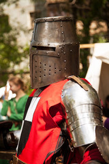 Naklejka premium Middle ages period costume at knight tournament. Medieval historical reenactment - a man wearing metal great helmet and red armor suit