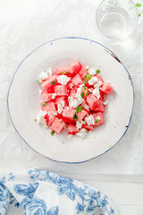 Fresh summer watermelon salad with feta cheese and greens on distressed white wooden background...