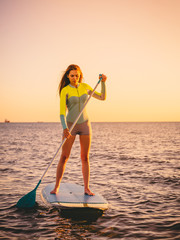 Sporty young girl stand up paddle surfing with beautiful sunset or sunrise colors