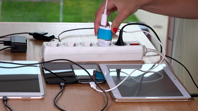Hand plugging various devices chargers to extension sockets on table
