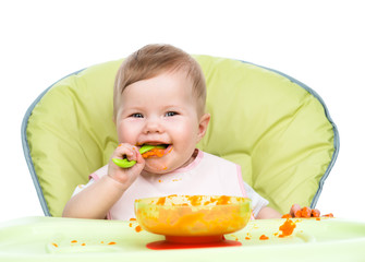 Happy baby sitting in high-chair with spoon and plate