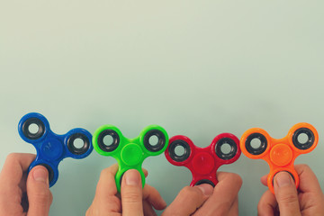 trendy fidget spinners - styled flat lay scene with hands holding generic design spinners on blue,...