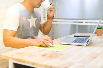 Asian man digital nomad drinking coffee and relax and working on a notebook computer for process clip VDO and design logo and update promotion for his friend in facebook in cafe shop