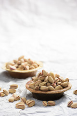 There are two brown wooden bowl filled with pistachio and  some have fallen out o fit and it has been shot on white background.