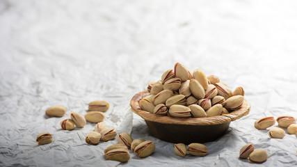  A heap of pistachios are in a wodden bowl and some pistachio are fallen around and its a close up shot clicked on white background. 