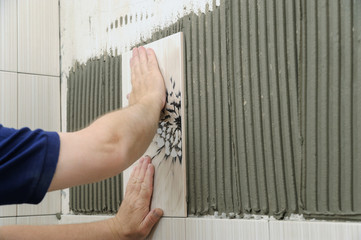 Tilers hands are  installing a ceramic tile.