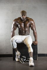 Fototapeta na wymiar Muscular Middle Eastern Black bodybuilder sits resting on a box wearing white tights 