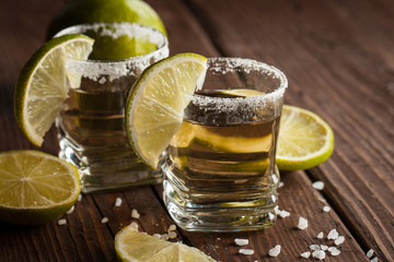 Macro focus photo of shots of golden Mexican tequila with lime and salt on wooden background....