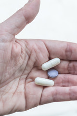 one hand holding white and purple pills, coated tablets,