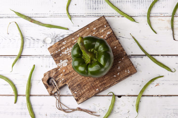 Green bell pepper on wooden cutting plank.