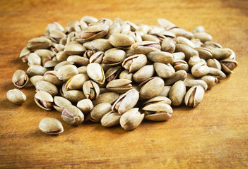 Salted pistachio nuts heap on wooden table with warm colors. Salty snack to beer