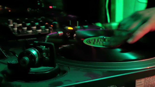 DJ puts a new record on the turntable. Outdoor party at night, colorful changing light.