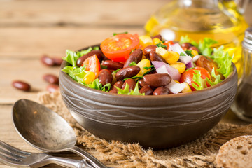 Fresh vegetable salad with beans in ceramic bowl on wooden table.