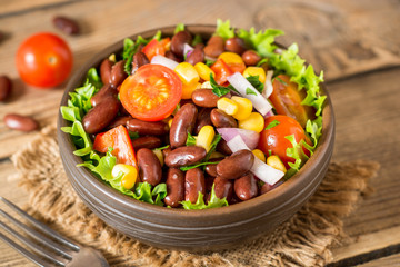 Fresh vegetable salad with beans in ceramic bowl on wooden table.