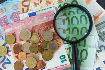 magnifying glass on pile of Euro banknotes with Euro coins as financial analysis concept