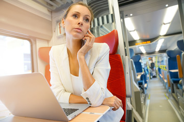 Businesswoman in train working on laptop and talking on phone