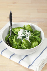 dumplings of spinach with sour cream and dill in a white plate with fork on white fabric with blue stripes