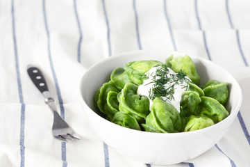 dumplings of spinach with sour cream and dill in a white plate with fork on white fabric with blue stripes