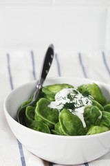 dumplings of spinach with sour cream and dill in a white plate with fork on white fabric with blue stripes