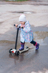 Little girl driving on kick scooter on the rainy road