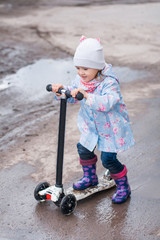 Little girl driving on kick scooter on the rainy road