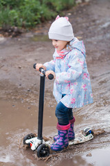 Little girl driving on kick scooter in the puddle