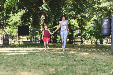 Beautiful young modern mom and her daughter walking through the park