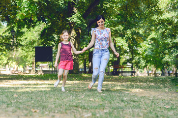 Naklejka na ściany i meble Beautiful young modern mom and her daughter walking through the park