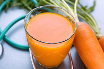 Glass of juice with fresh carrot and stethoscope on grey background. Health care concept