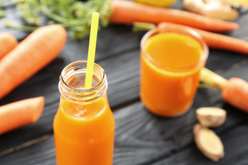 Bottle of juice with fresh carrot on wooden background