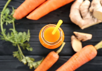 Bottle of juice with fresh carrot and ginger on wooden background