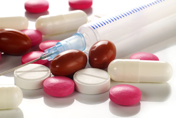 small pile of assorted pills and tablets and syringe on white background