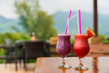 Two glasses with a Fruit soft cocktail made from fresh watermelon and blueberries on a glass table in the background of a tropical landscape. Luxurious vacation.