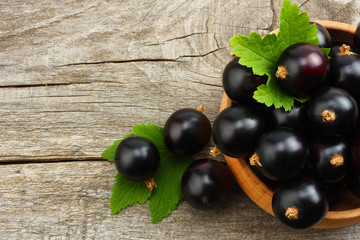 black currant in wooden bowl with green leaf on old wooden background. top view
