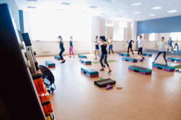 In the foreground a sports projectile disc for a bar, in the background a group of girls of friends are engaged in fitness. Sports hall concept gym. Glare sun