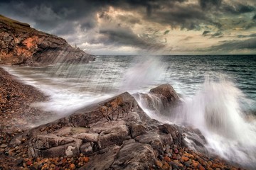 Obraz premium Slow shutter speed showing the movement of a wave crashing on Bracelet Bay on the Gower peninsula, Swansea, South Wales.
