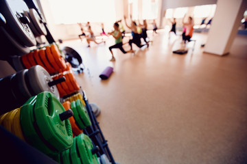 Obraz premium In the foreground a sports projectile disc for a bar, in the background a group of girls of friends are engaged in fitness. Sports hall concept gym. Glare sun
