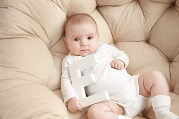 Cute baby with letter E lying in armchair. Choosing name concept